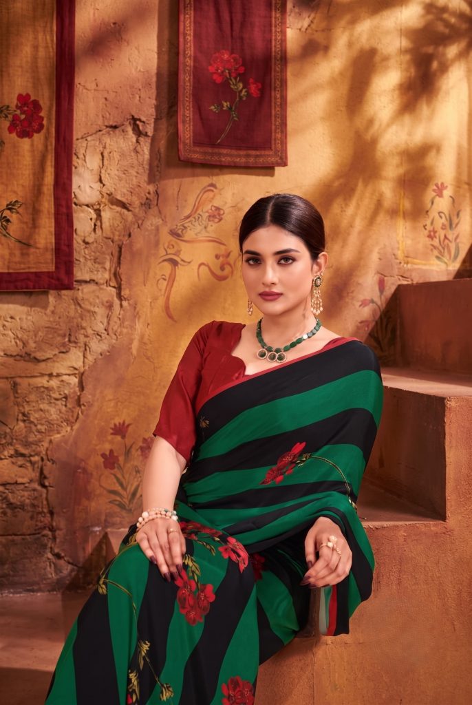 Woman seated on steps wearing a green and black striped saree with floral prints and a maroon blouse.