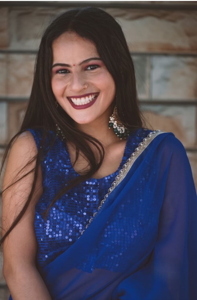 Smiling South Asian woman wearing a royal blue sequined saree blouse with traditional dangling earrings.
